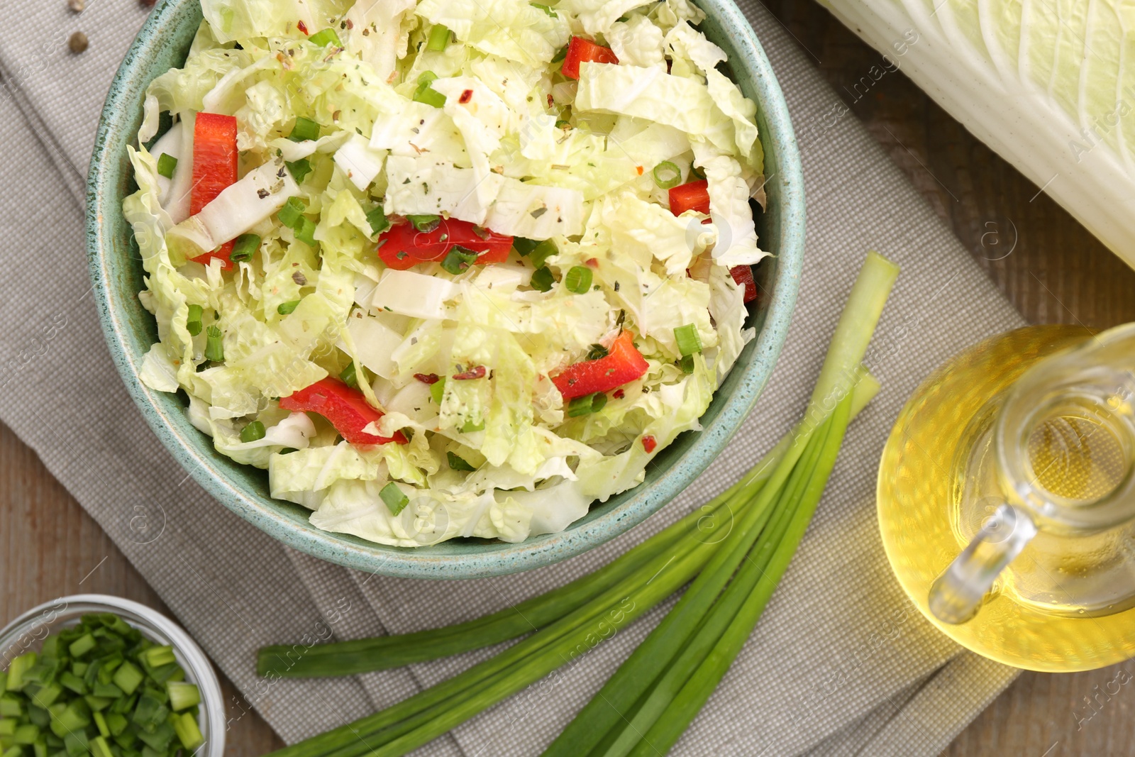 Photo of Tasty salad with Chinese cabbage in bowl, oil and green onion on wooden table, flat lay