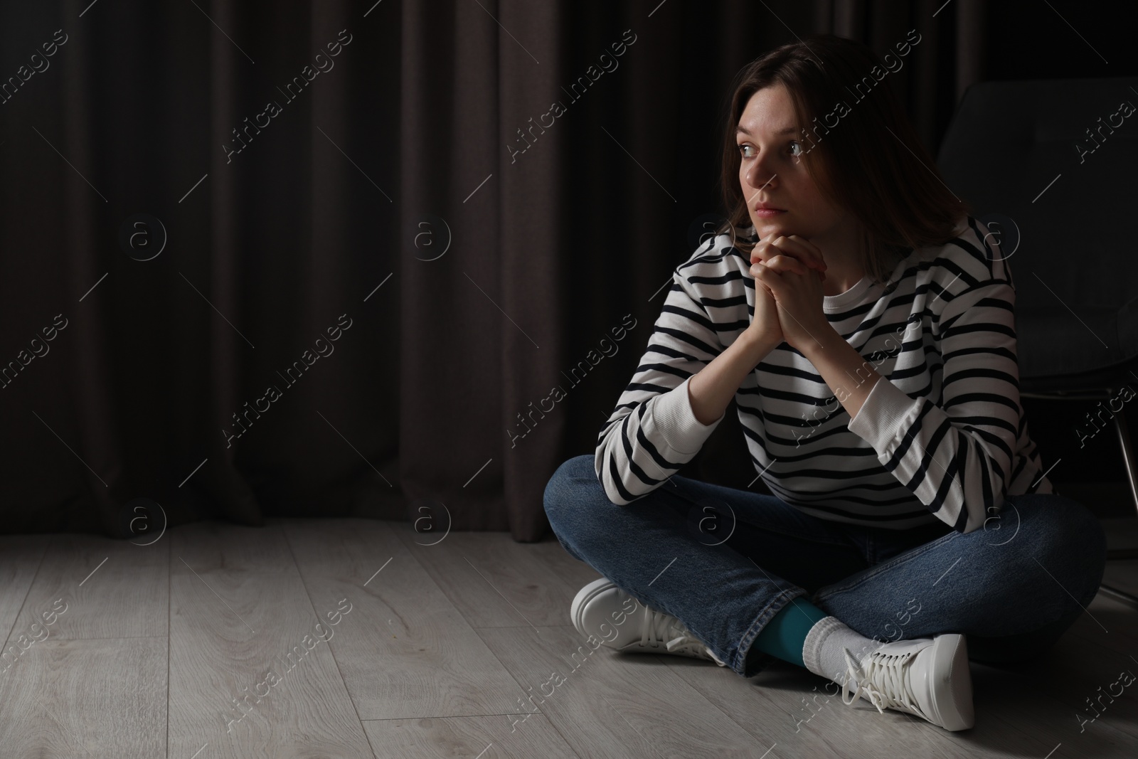 Photo of Sad young woman sitting on floor indoors, space for text