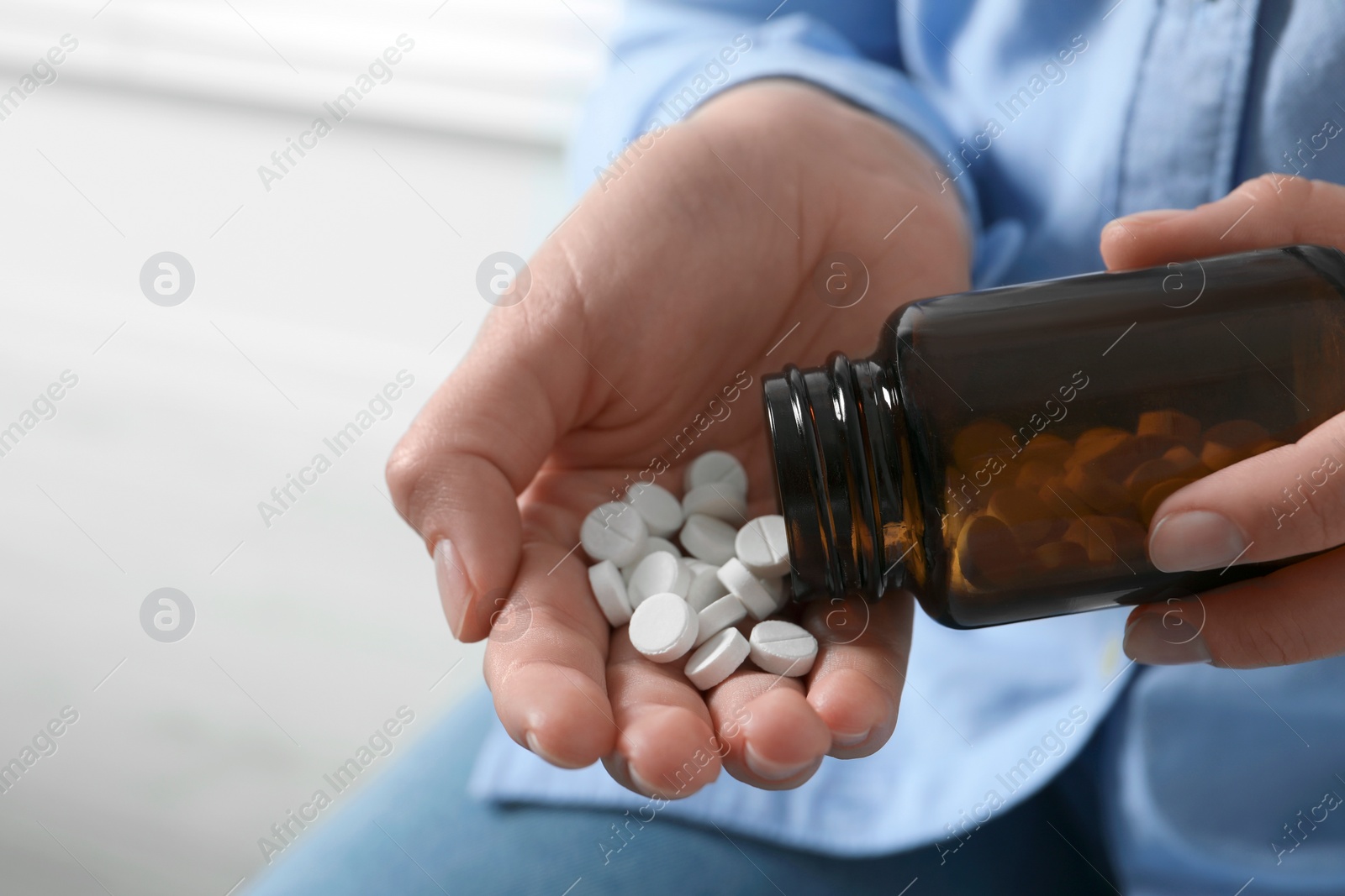 Photo of Woman pouring pills from bottle on blurred background, closeup