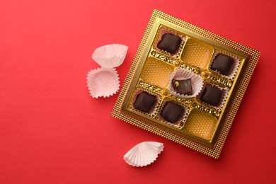 Photo of Partially empty box of chocolate candies on red background, top view. Space for text