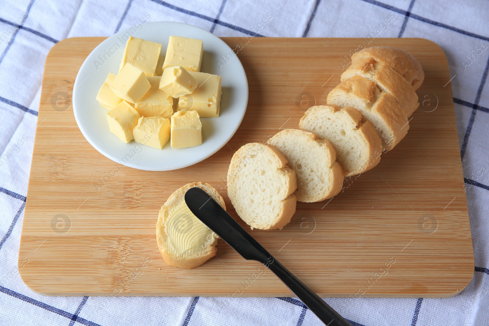 Photo of Cut baguette with fresh butter on checkered tablecloth, closeup