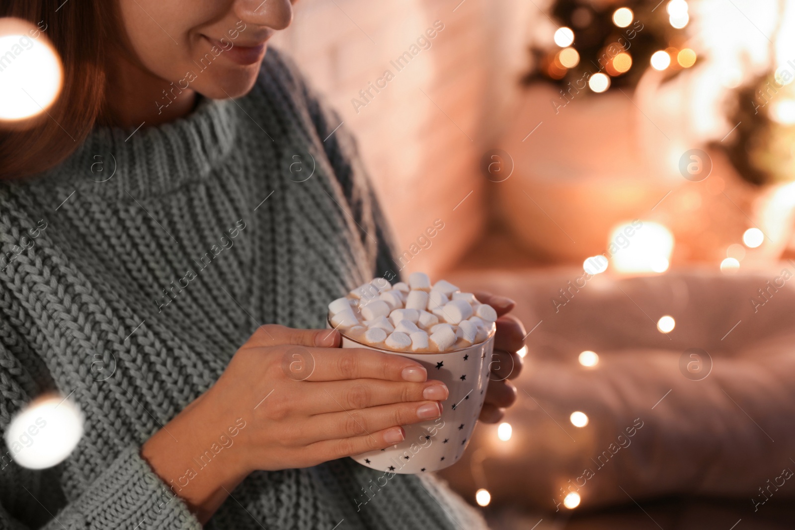 Photo of Woman holding cup of hot drink with marshmallows indoors, closeup. Magic Christmas atmosphere