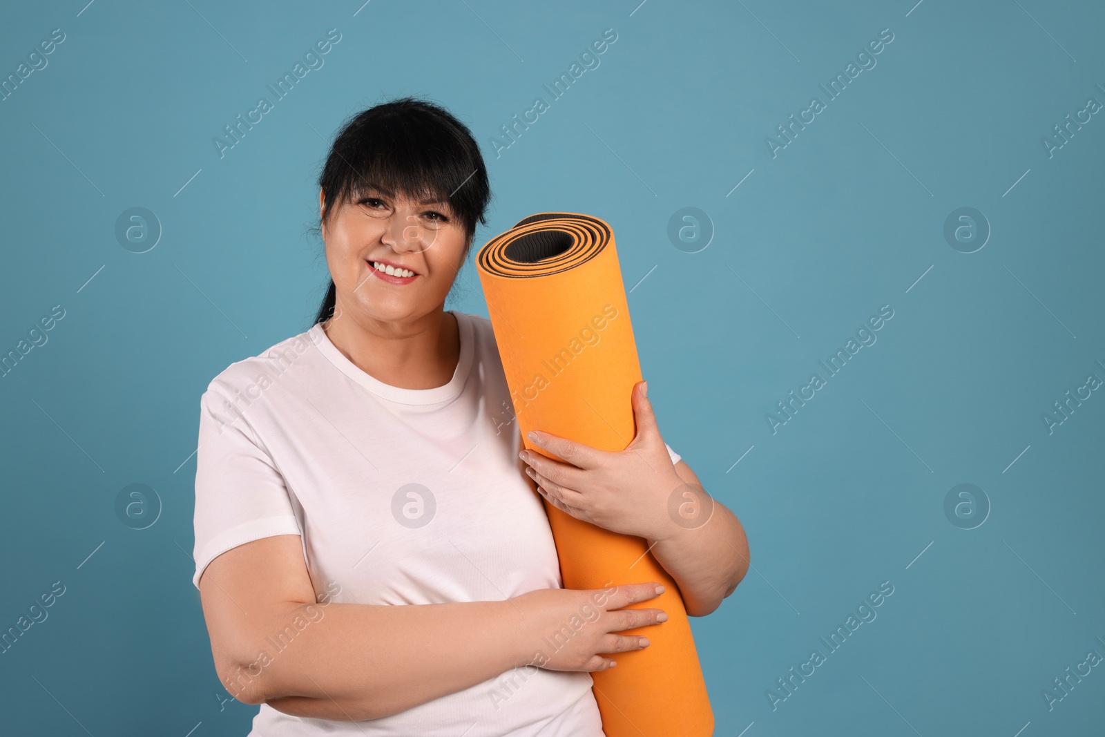 Photo of Happy overweight mature woman with yoga mat on light blue background. Space for text