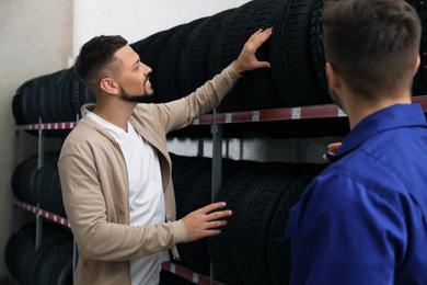 Mechanic helping client to choose car tire in auto store