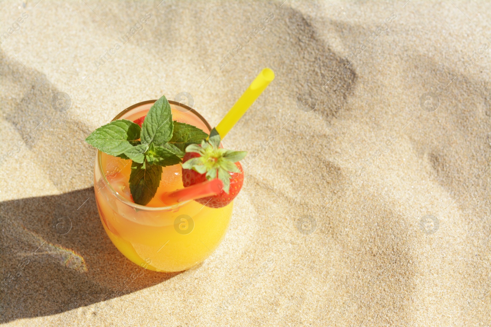 Photo of Glass of refreshing drink with strawberry on sandy beach, above view. Space for text