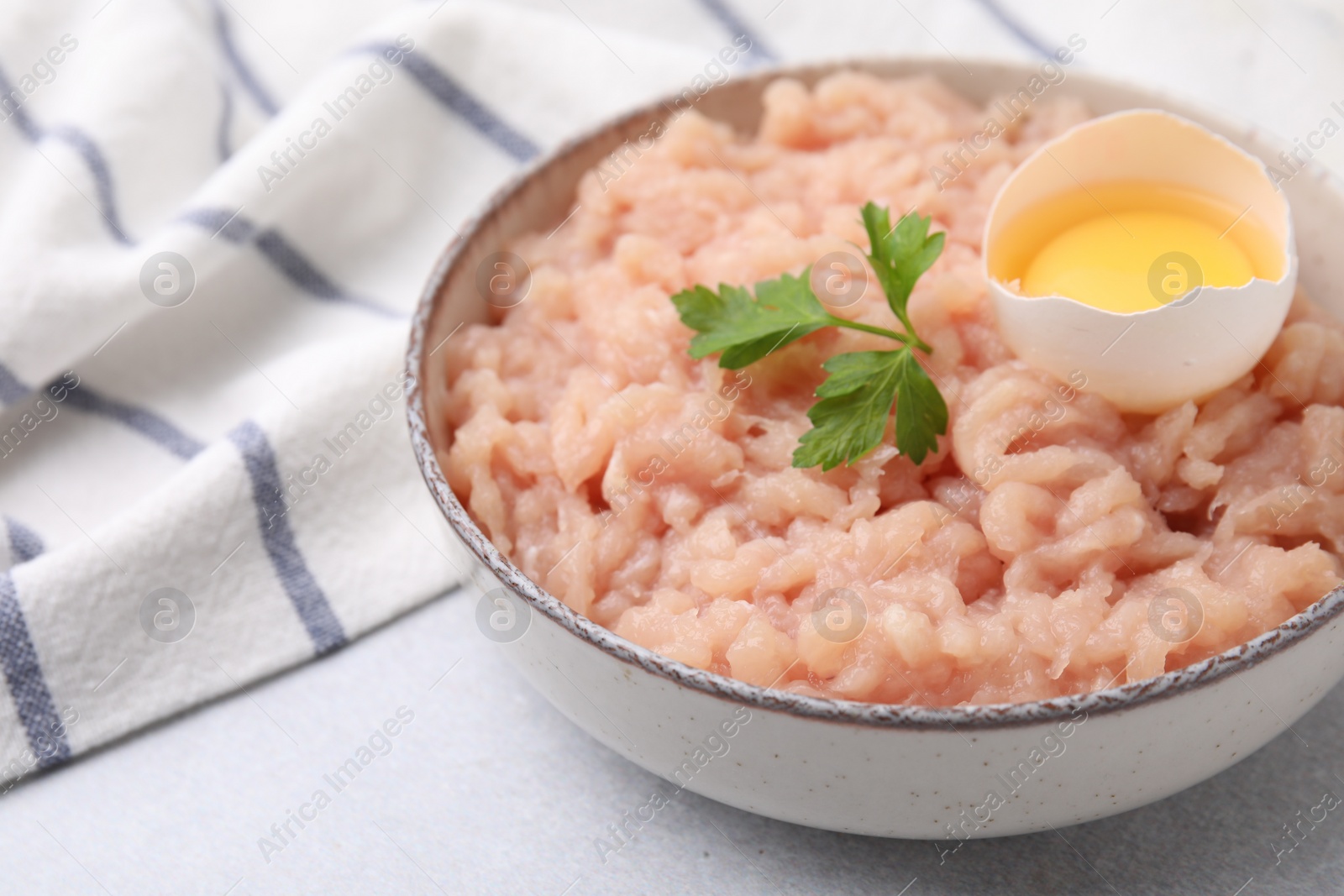 Photo of Fresh raw minced meat, parsley and egg in bowl on light grey table, closeup. Space for text