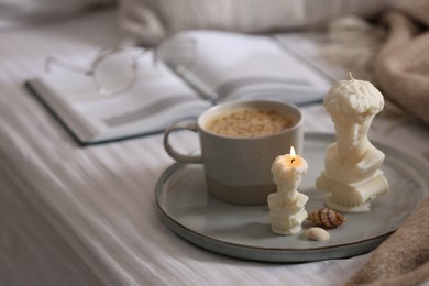 Photo of Beautiful David bust candles, seashells and cup of hot drink on bed indoors, space for text