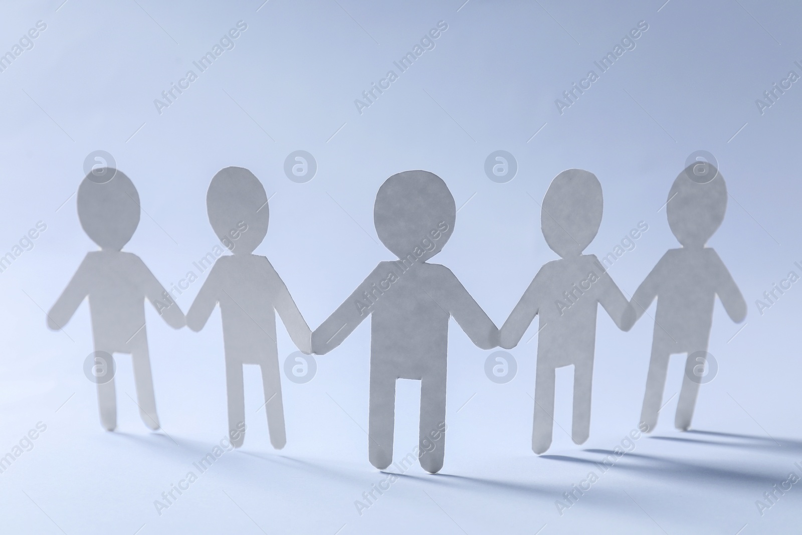 Photo of Teamwork concept. Paper figures of people holding hands on light grey background, closeup