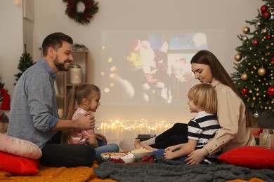 Photo of Happy family spending time together near video projector in cosy room. Christmas atmosphere