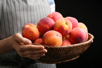 Photo of Woman with fresh sweet peaches in wicker bowl, closeup