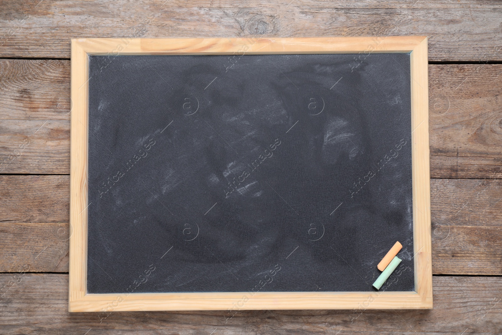 Photo of Blackboard with pieces of color chalk on wooden background, top view. Space for text