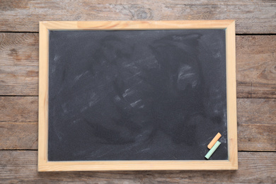 Photo of Blackboard with pieces of color chalk on wooden background, top view. Space for text
