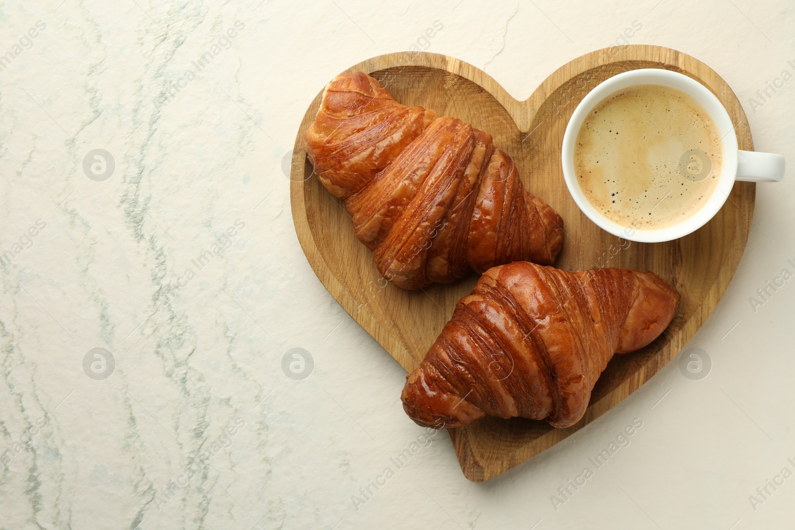 Photo of Tasty croissants served with cup of hot drink on light textured table, top view. Space for text
