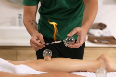 Photo of Therapist giving fire cupping treatment to patient in spa salon, closeup