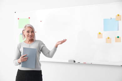 Photo of Mature teacher with notebook near whiteboard in classroom. Space for text