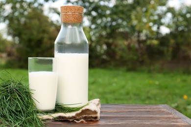 Photo of Tasty fresh milk and green grass on wooden table. Space for text