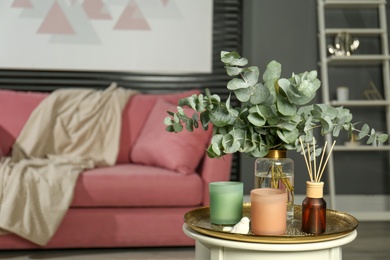 Eucalyptus branches, aromatic reed air freshener and candles on table in living room, space for text. Interior element