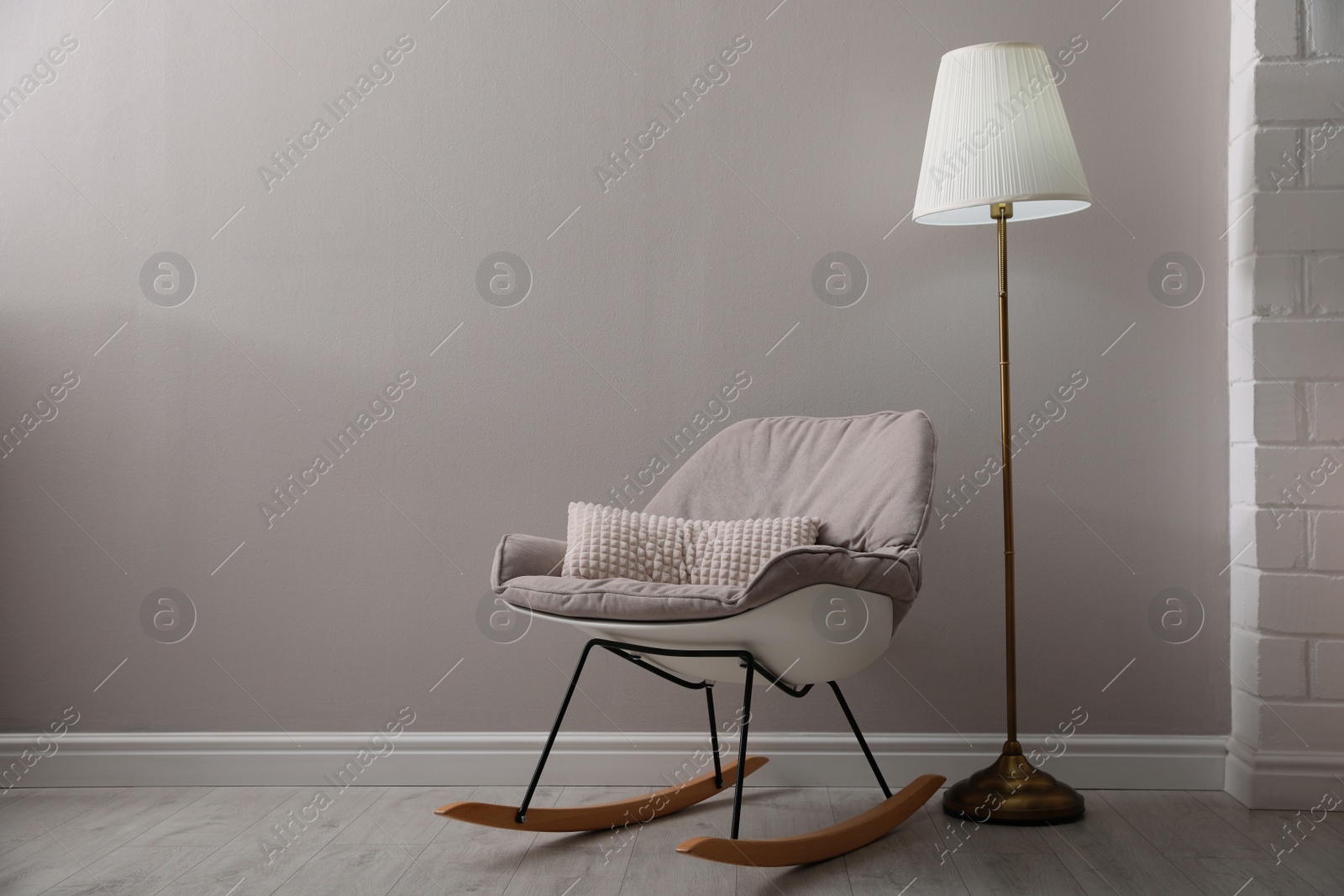 Photo of Comfortable rocking chair and lamp near light grey wall indoors, space for text