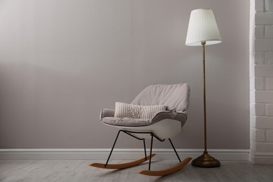 Photo of Comfortable rocking chair and lamp near light grey wall indoors, space for text