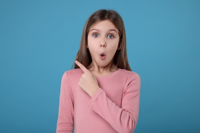 Surprised girl pointing at something on light blue background