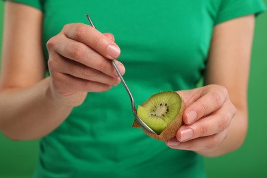 Photo of Woman eating kiwi with spoon on green background, closeup