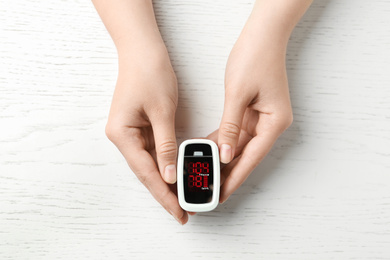 Photo of Woman holding fingertip pulse oximeter on white wooden background, top view