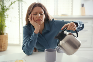 Photo of Sleepy young woman pouring coffee into cup at home in morning