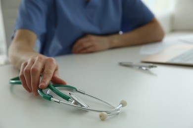 Photo of Doctor with stethoscope at white table in hospital, closeup
