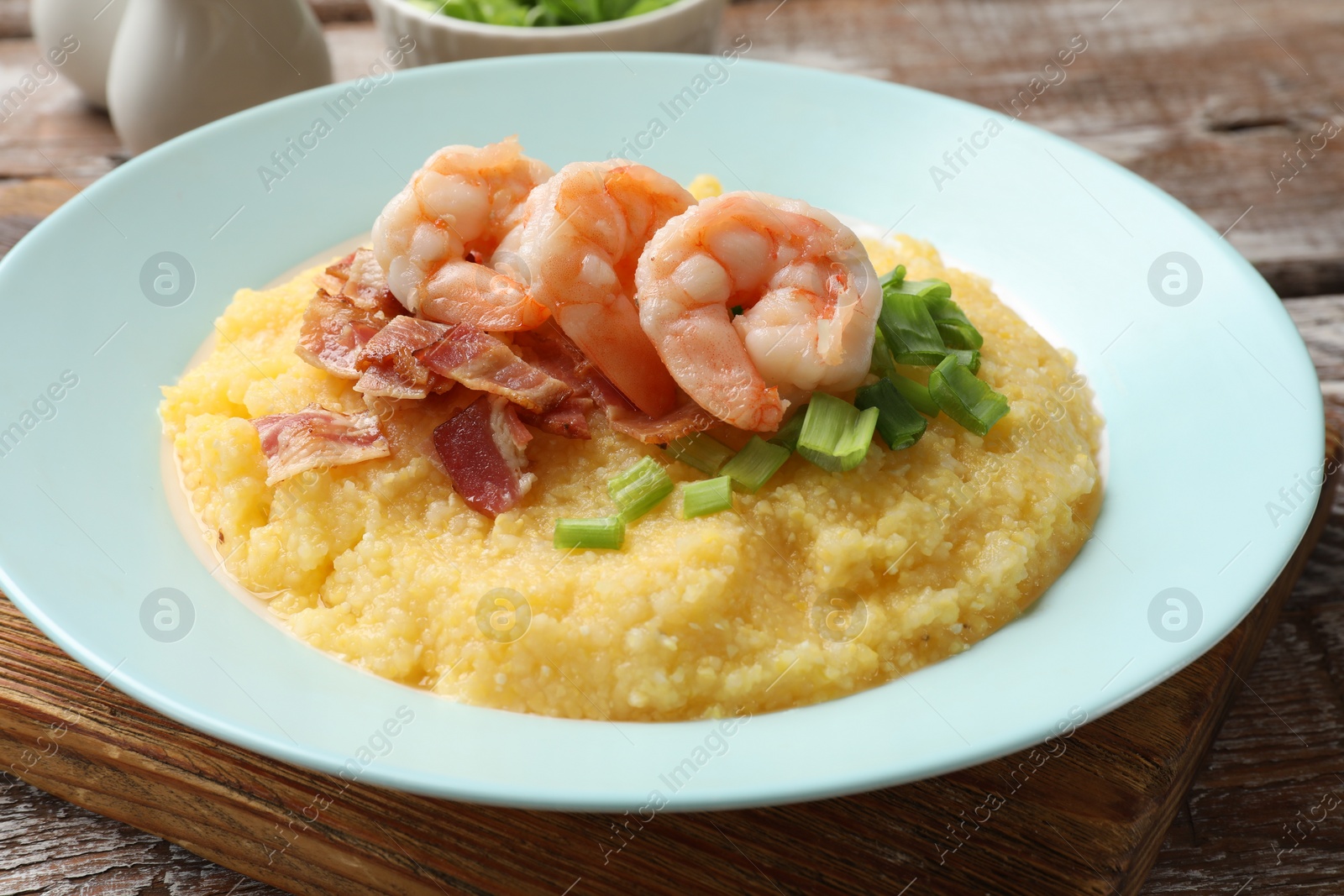 Photo of Plate with fresh tasty shrimps, bacon, grits and green onion on wooden table, closeup