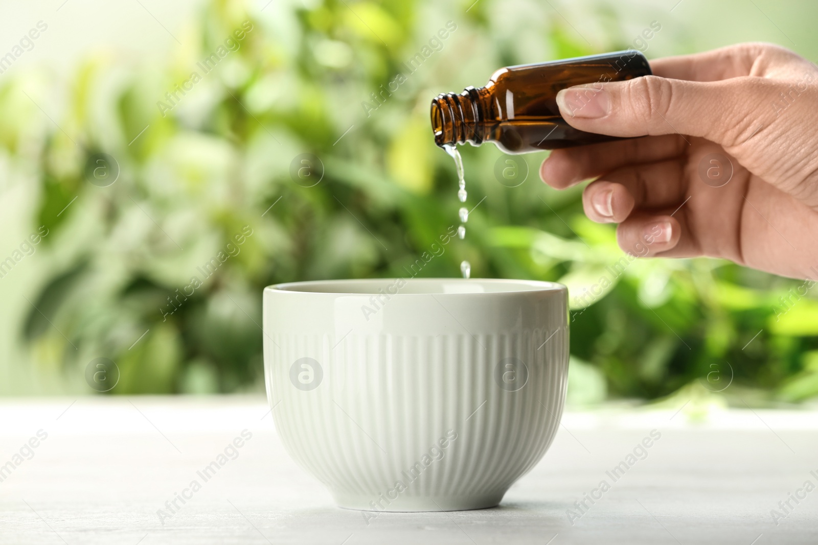 Photo of Woman pouring essential oil from bottle into bowl on table