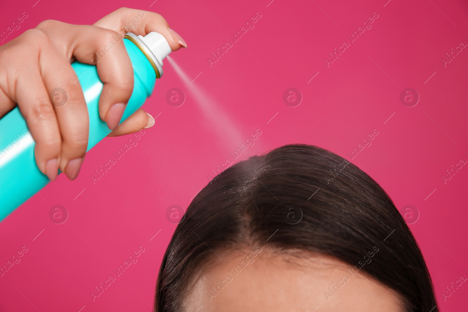 Photo of Young woman applying dry shampoo against pink background, closeup