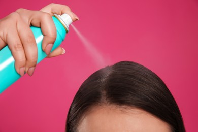 Photo of Young woman applying dry shampoo against pink background, closeup