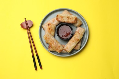 Photo of Fried spring rolls and sauce served on yellow table, top view