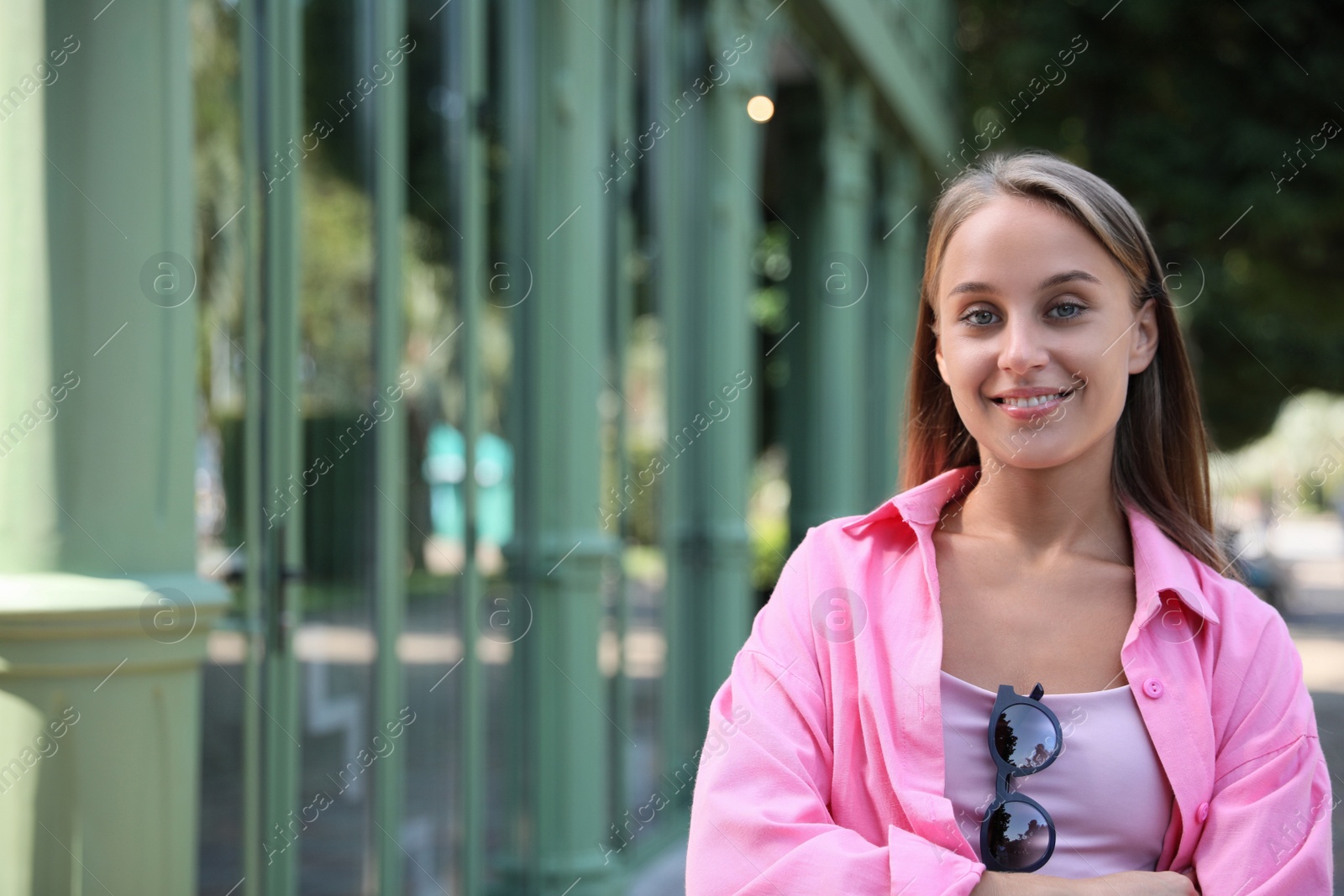 Photo of Beautiful young woman with stylish sunglasses near building outdoors, space for text