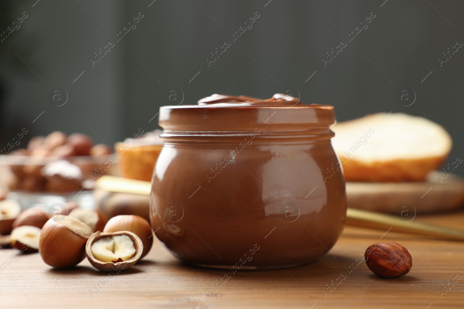 Photo of Glass jar with tasty chocolate hazelnut spread and nuts on wooden table