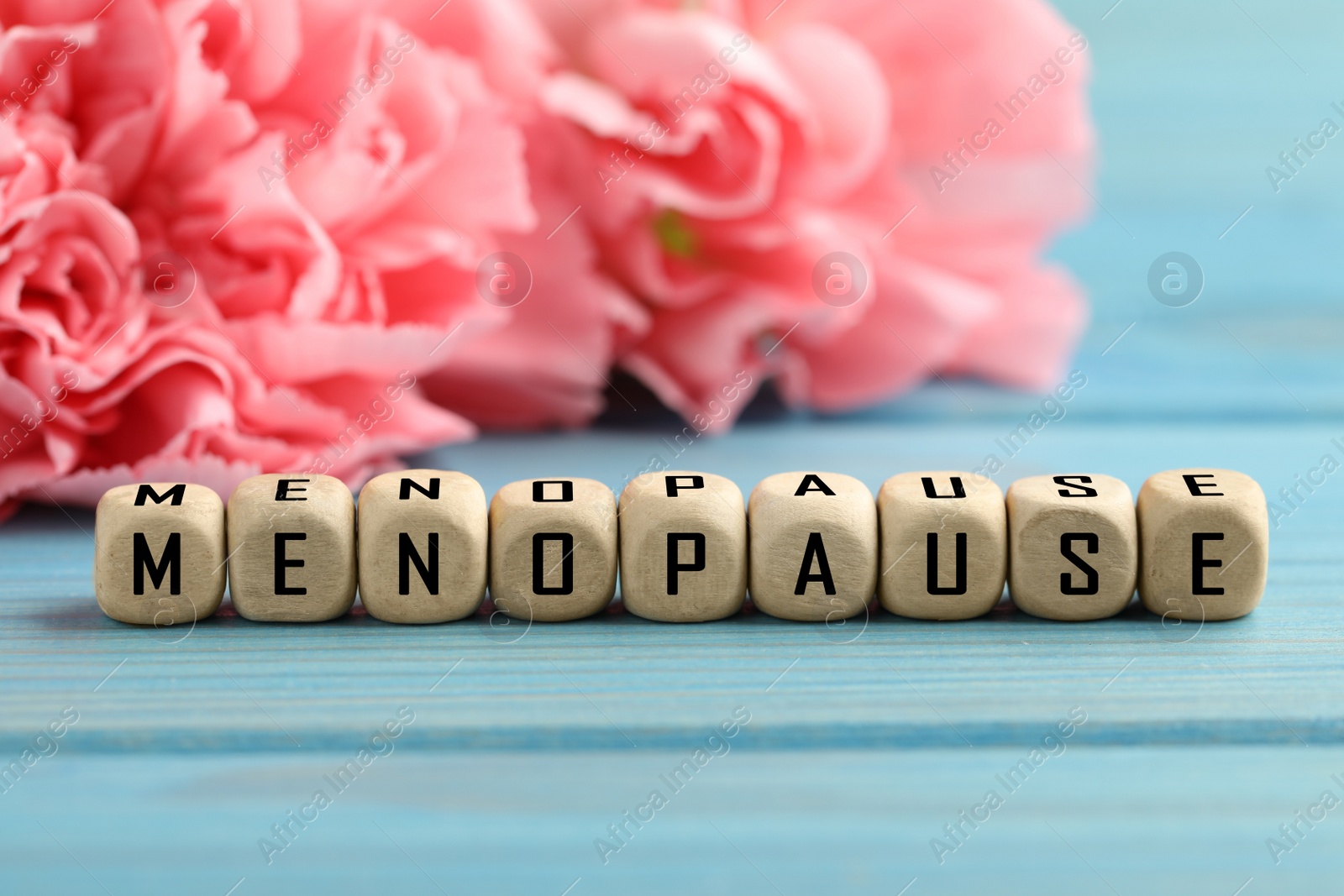 Photo of Wooden cubes with word Menopause and beautiful carnation flowers on turquoise background