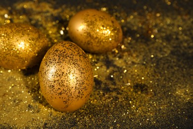 Photo of Shiny golden eggs with glitter on dark table, space for text