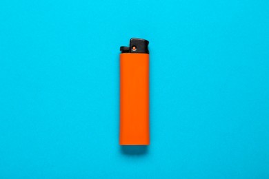 Photo of Orange plastic cigarette lighter on light blue background, top view