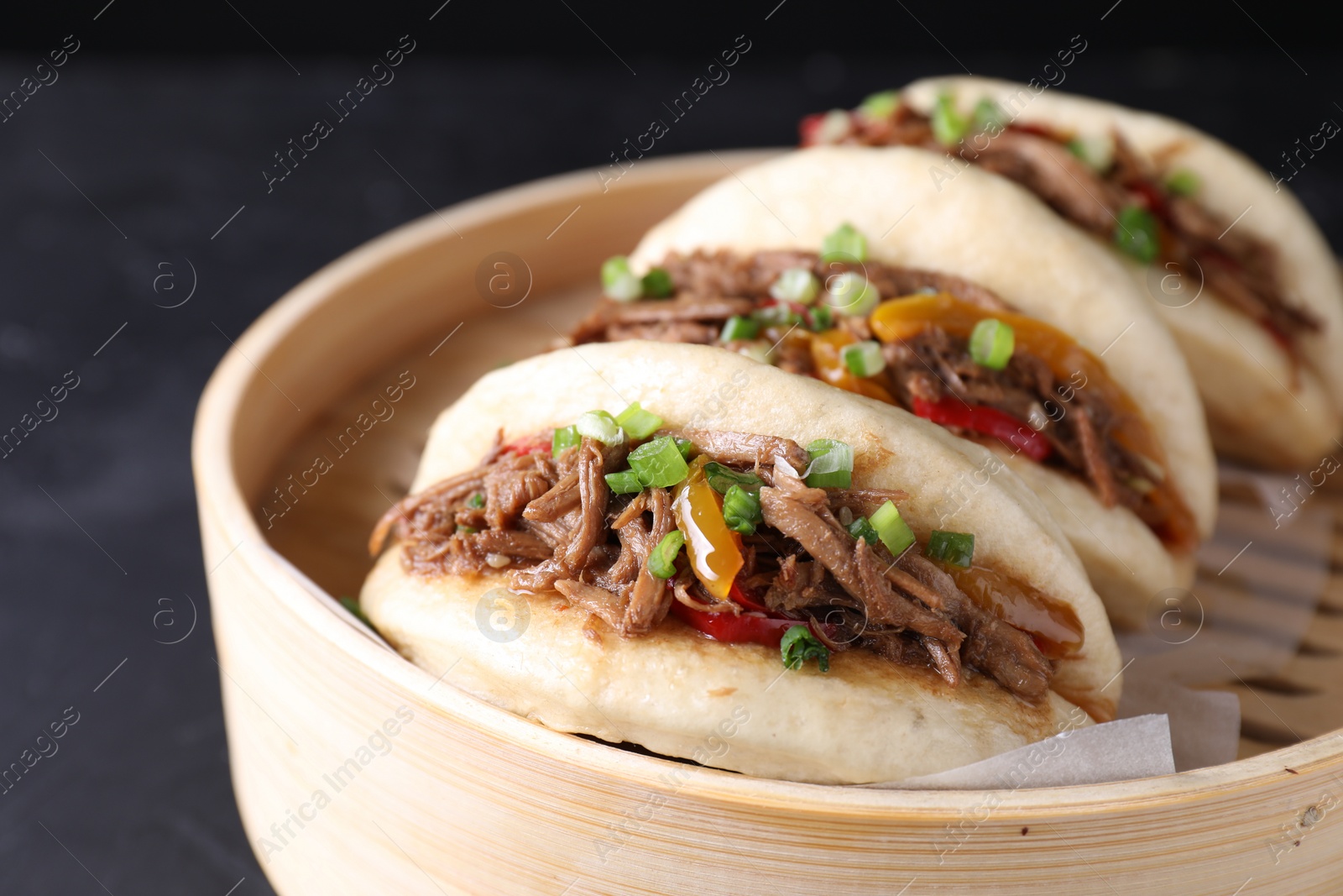 Photo of Delicious gua bao in bamboo steamer on black table, closeup