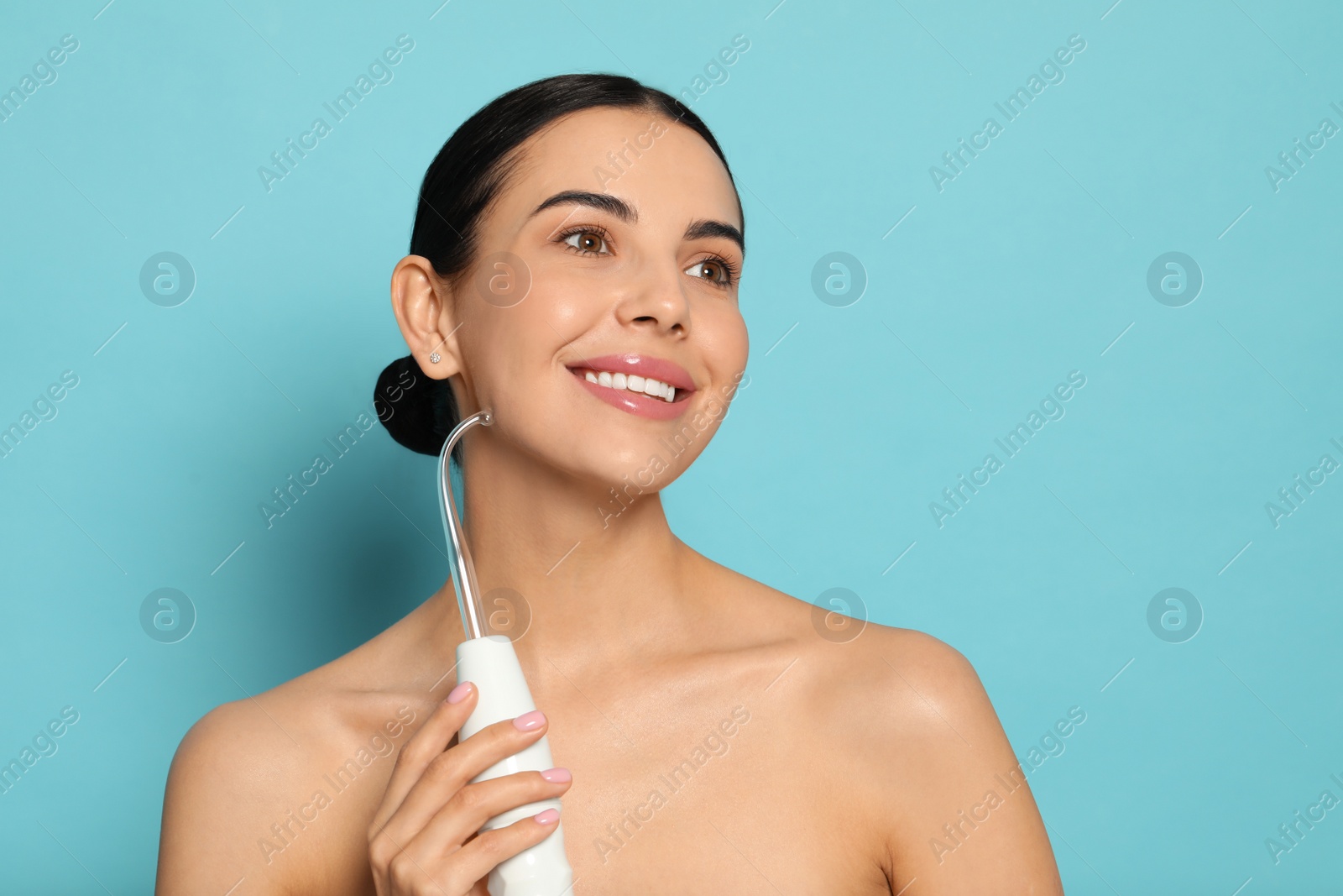 Photo of Woman using high frequency darsonval device on light blue background. Space for text