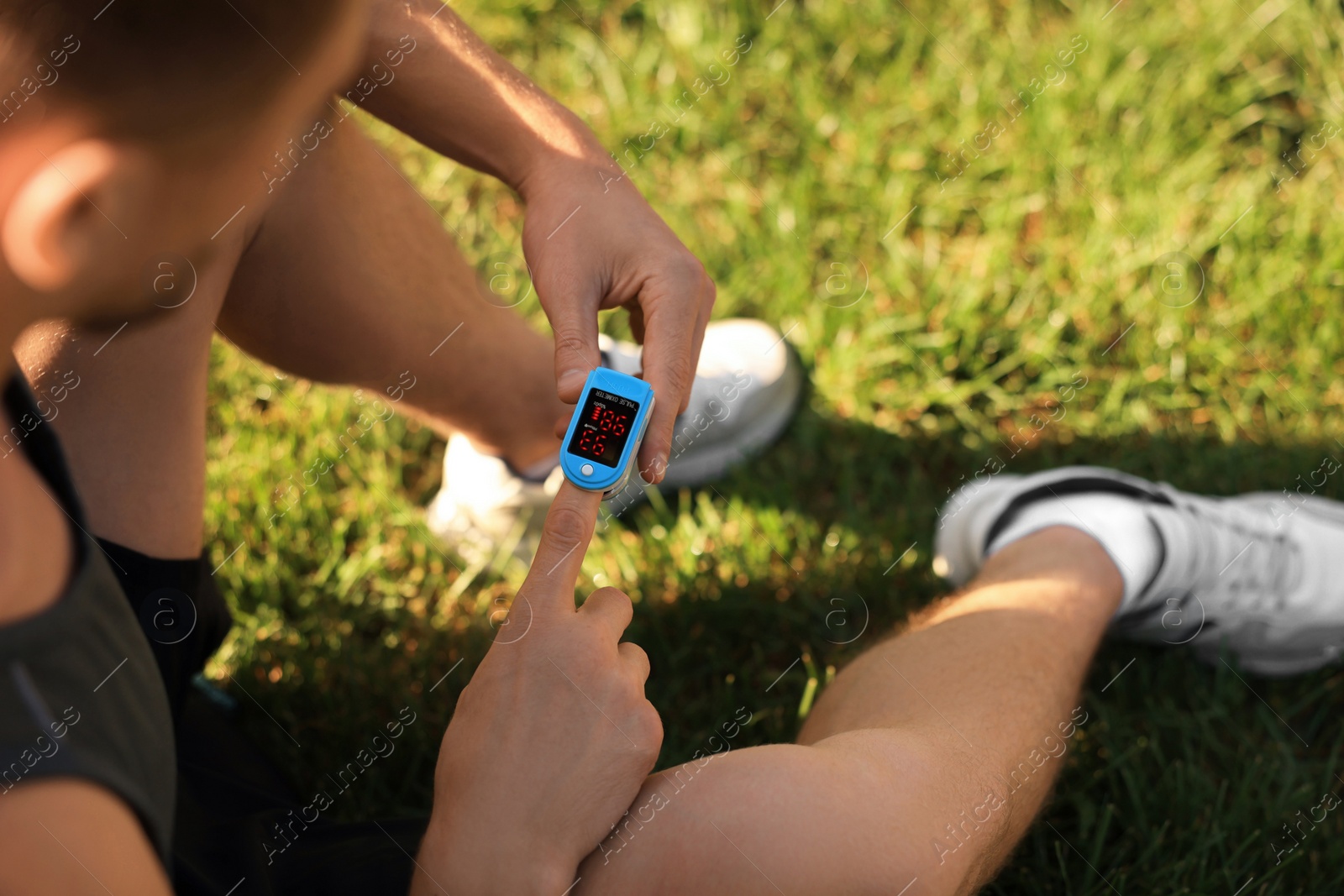 Photo of Man checking pulse with blood pressure monitor on finger after training outdoors, closeup