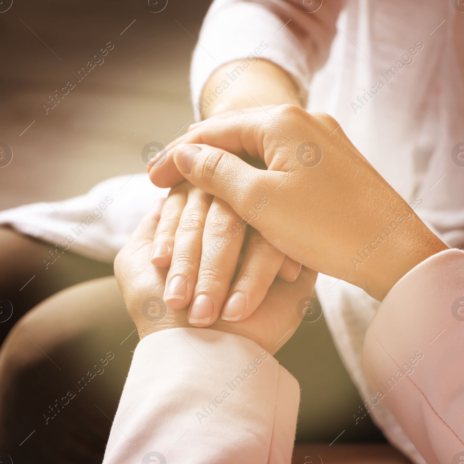 Image of Volunteer holding hands with woman in sunlit room, closeup