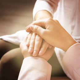 Image of Volunteer holding hands with woman in sunlit room, closeup