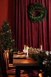 Dining table with burning candles and Christmas decor in stylish room. Interior design