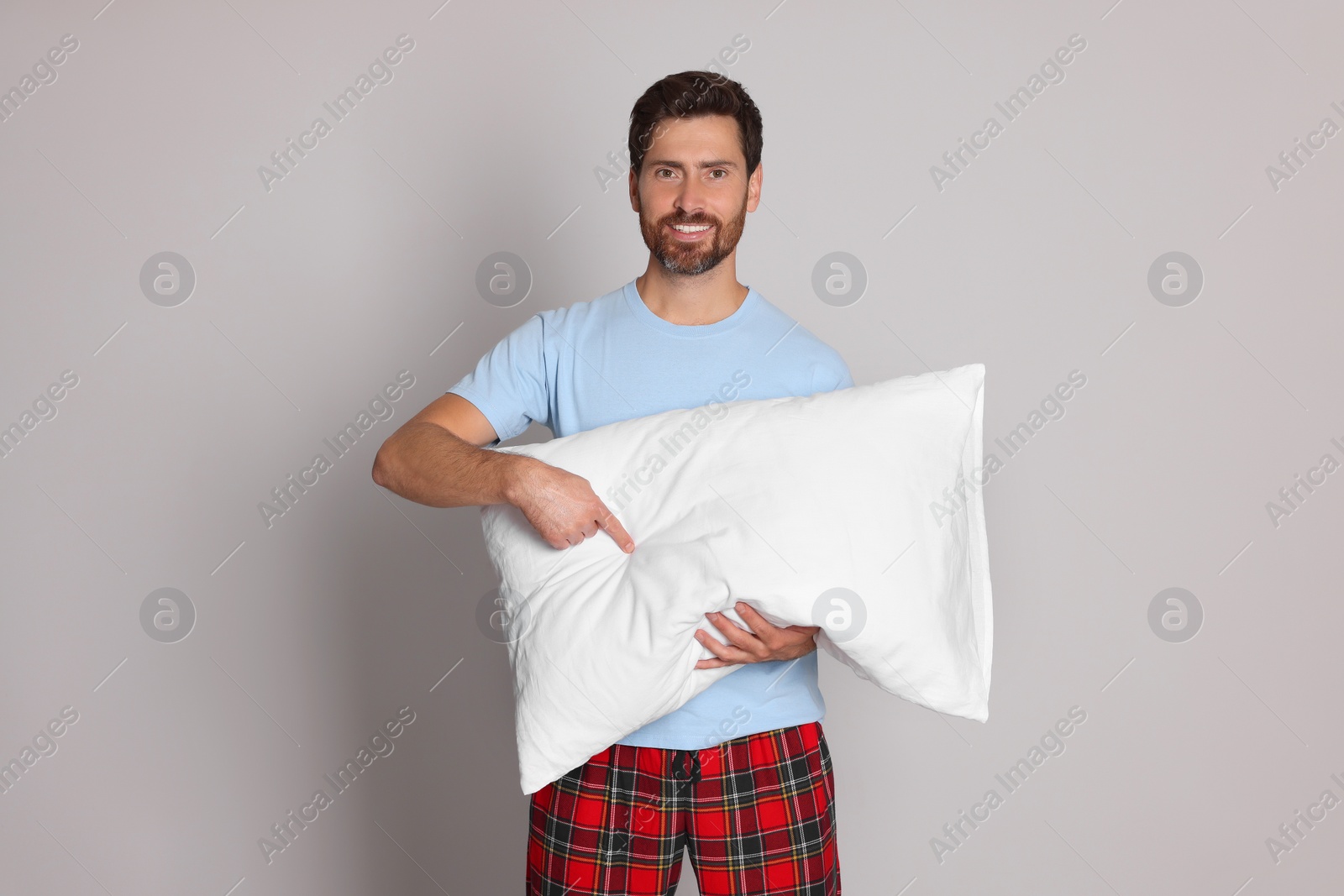 Photo of Smiling handsome man pointing on soft pillow against light grey background