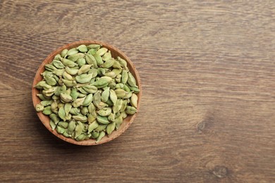 Photo of Bowl of dry cardamom pods on wooden table, top view. Space for text