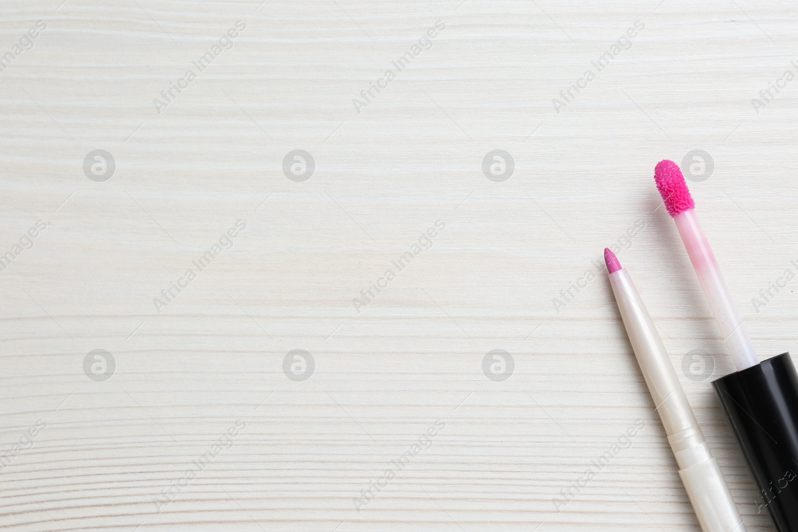 Photo of Bright lip pencil and brush of liquid lipstick on white wooden table, flat lay. Space for text