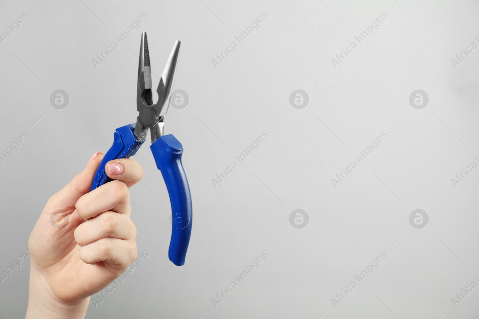 Photo of Woman with needle nose pliers on grey background, closeup. Space for text