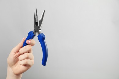 Photo of Woman with needle nose pliers on grey background, closeup. Space for text
