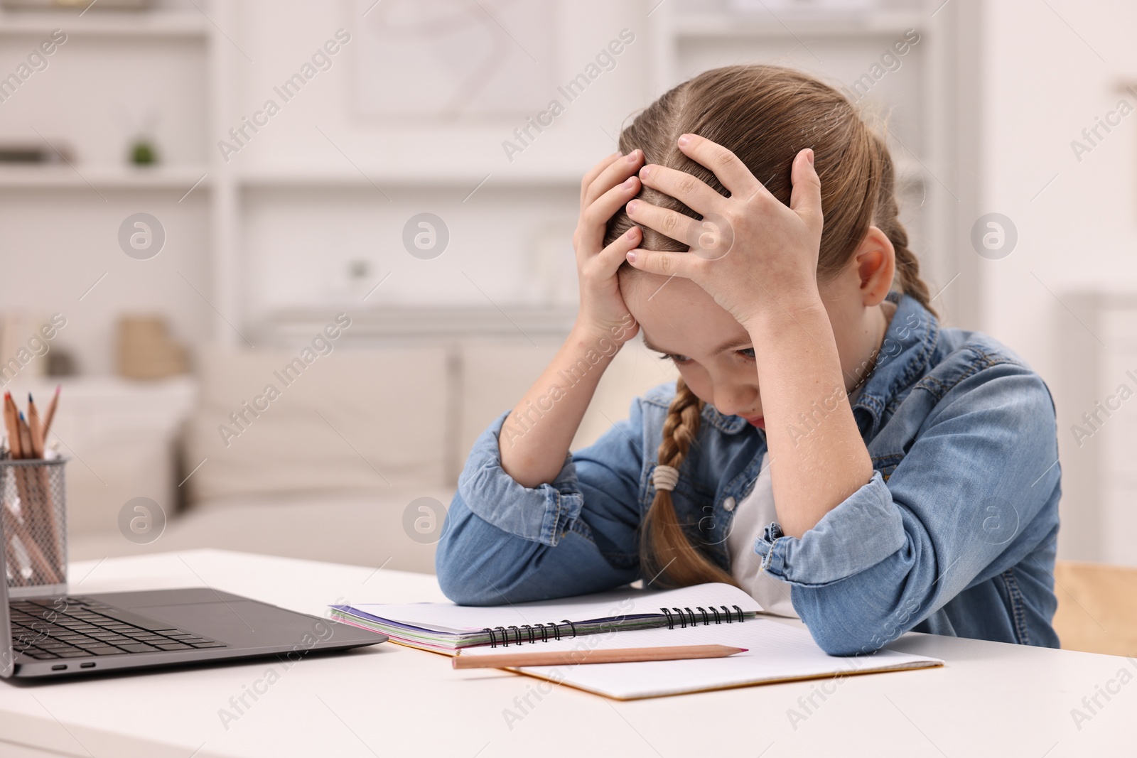 Photo of Little girl suffering from headache while doing homework at home